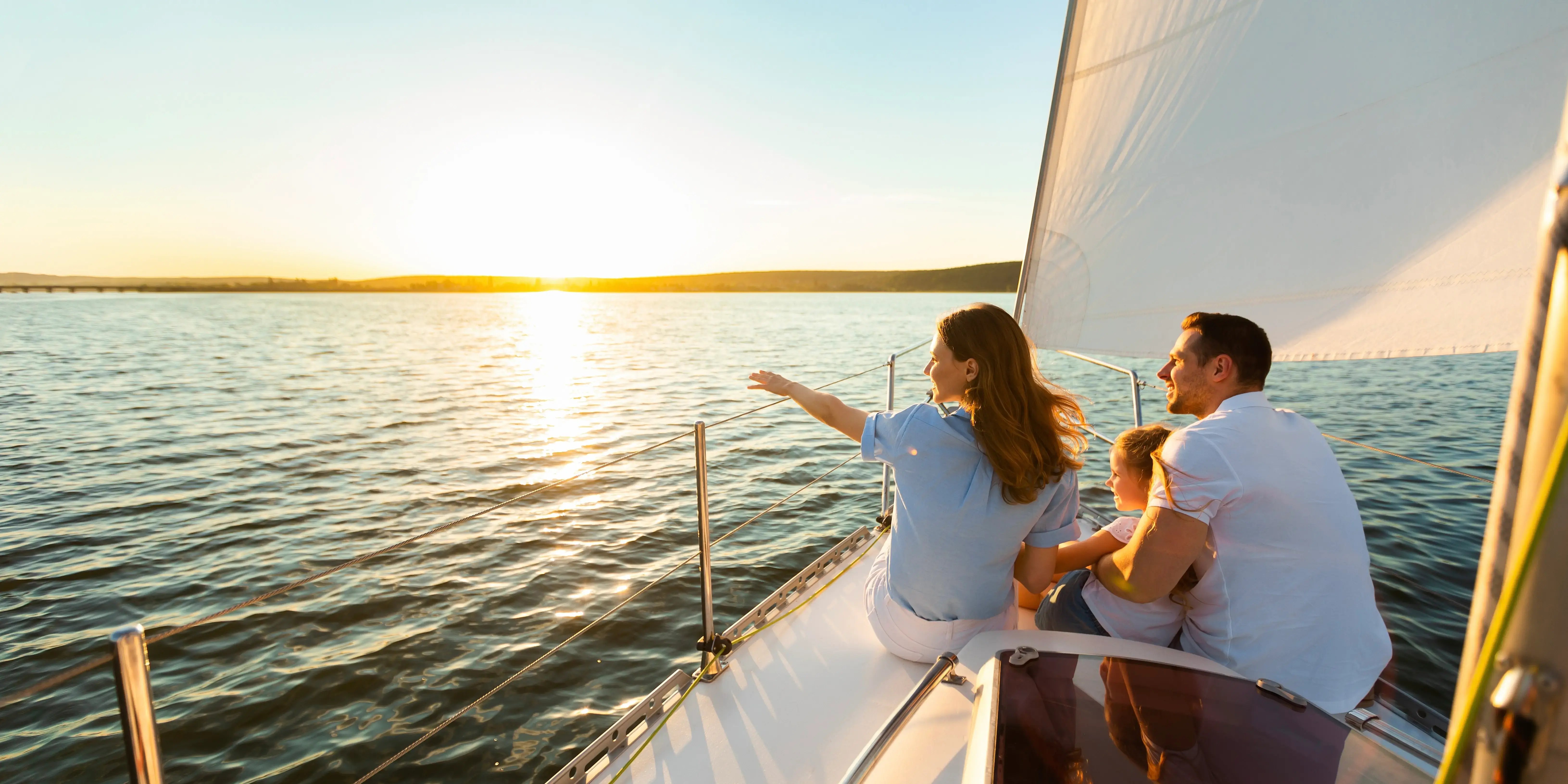 Familia de tres navegando en yate sentados en la cubierta del velero mirando la puesta de sol en la costa para vivir el lujo con estrategia