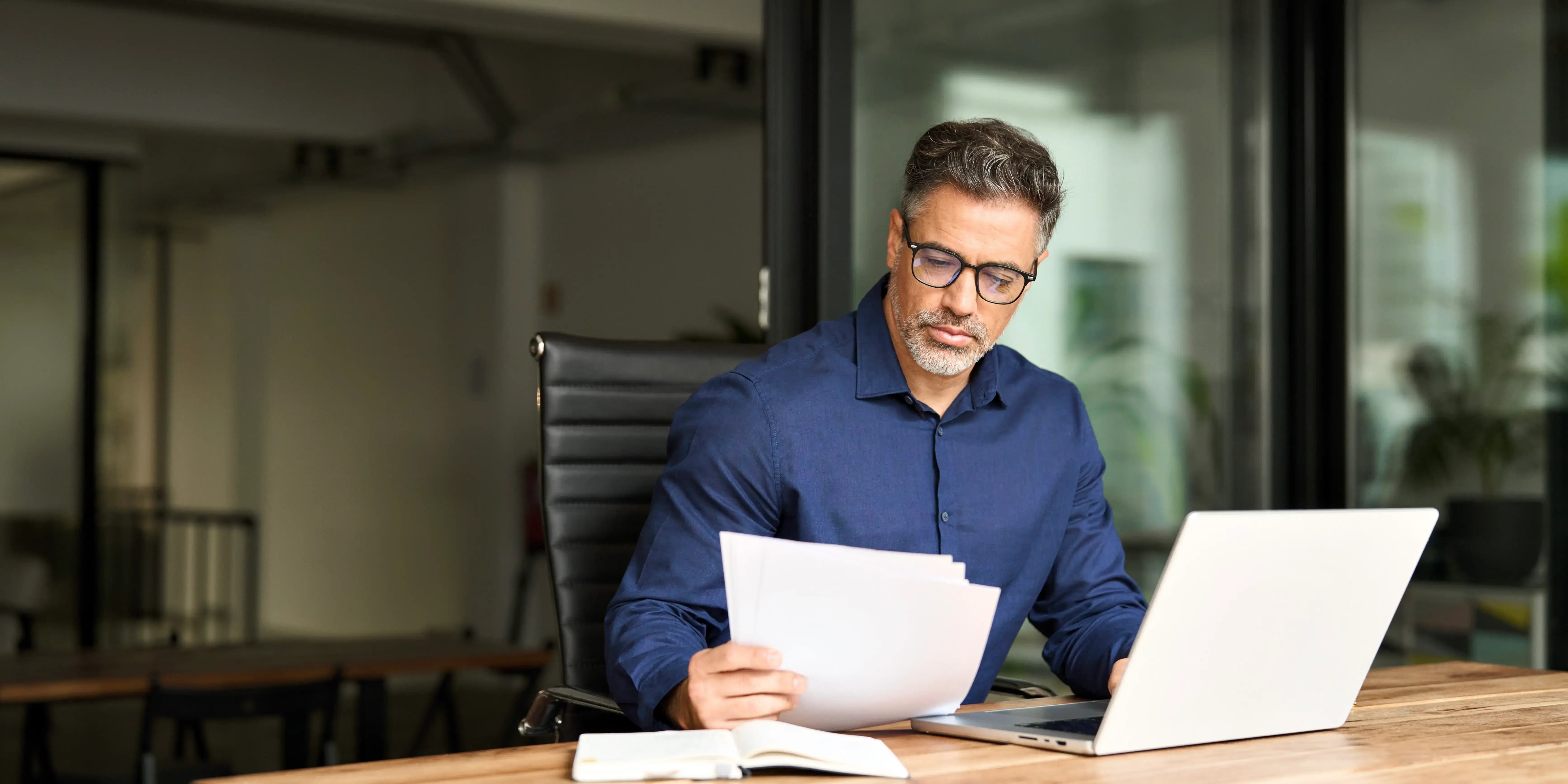 Hombre con una computadora y concentrado con documentos de cuentas bancarias, créditos, ingresos y bienes inmuebles para realizar la declaración patrimonial