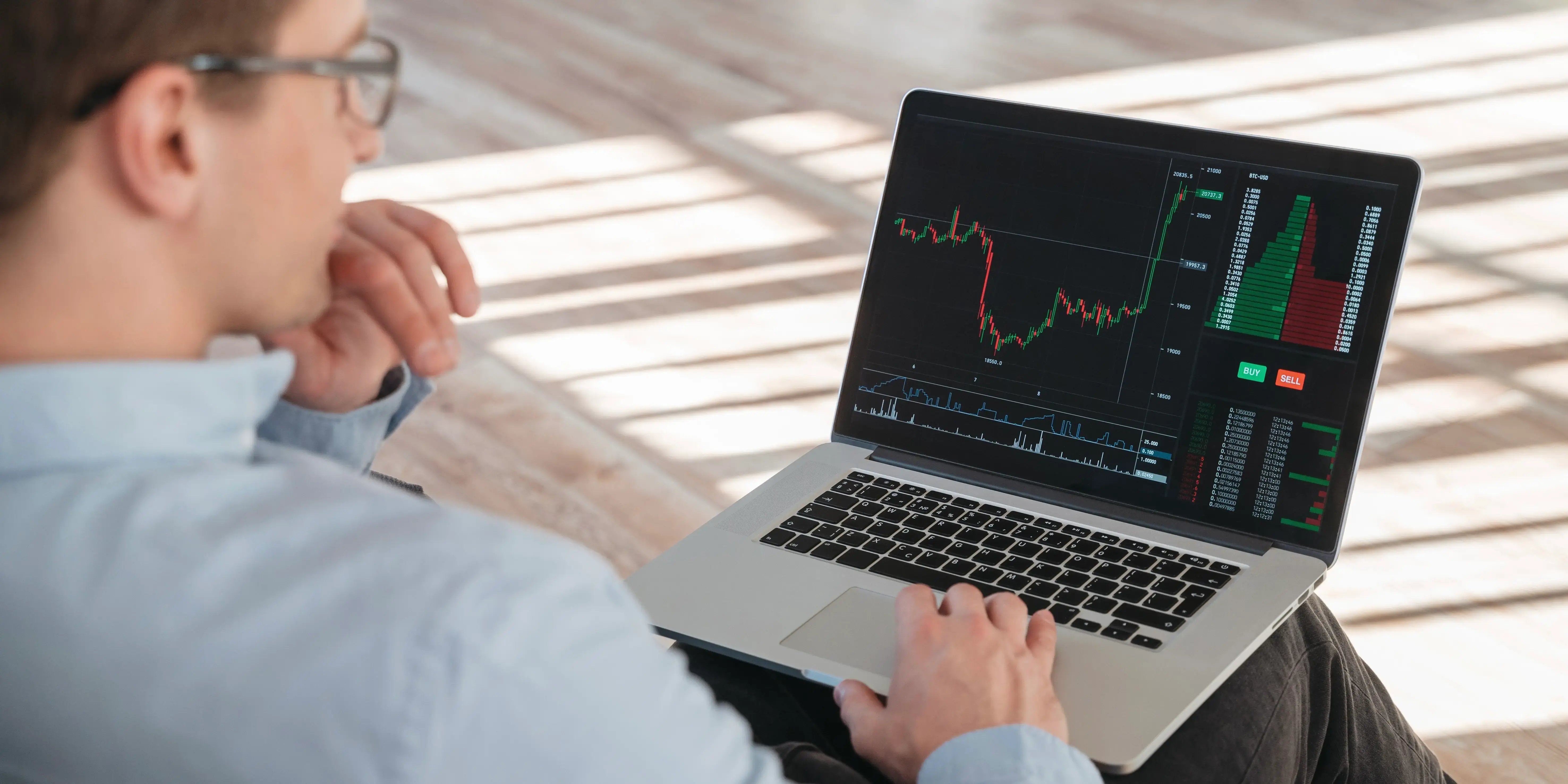 Hombre sentado con una computadora en las piernas analizando las graficas de sus inversiones a corto plazo
