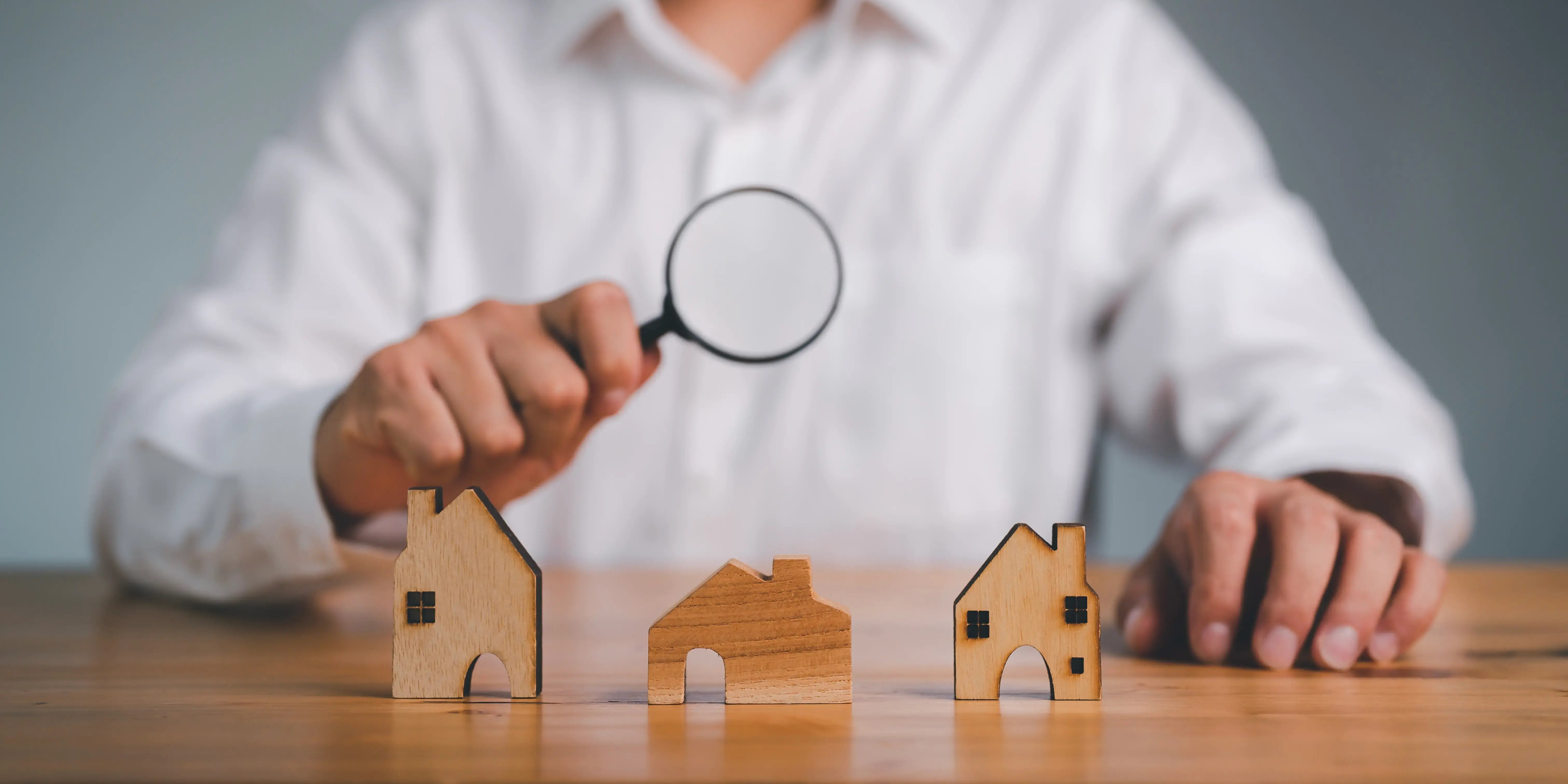 Mano usando lupa para buscar errores cobre 3 casas de modelo en miniatura y elegir la mejor opción de ubicación para comprar casa o departamento