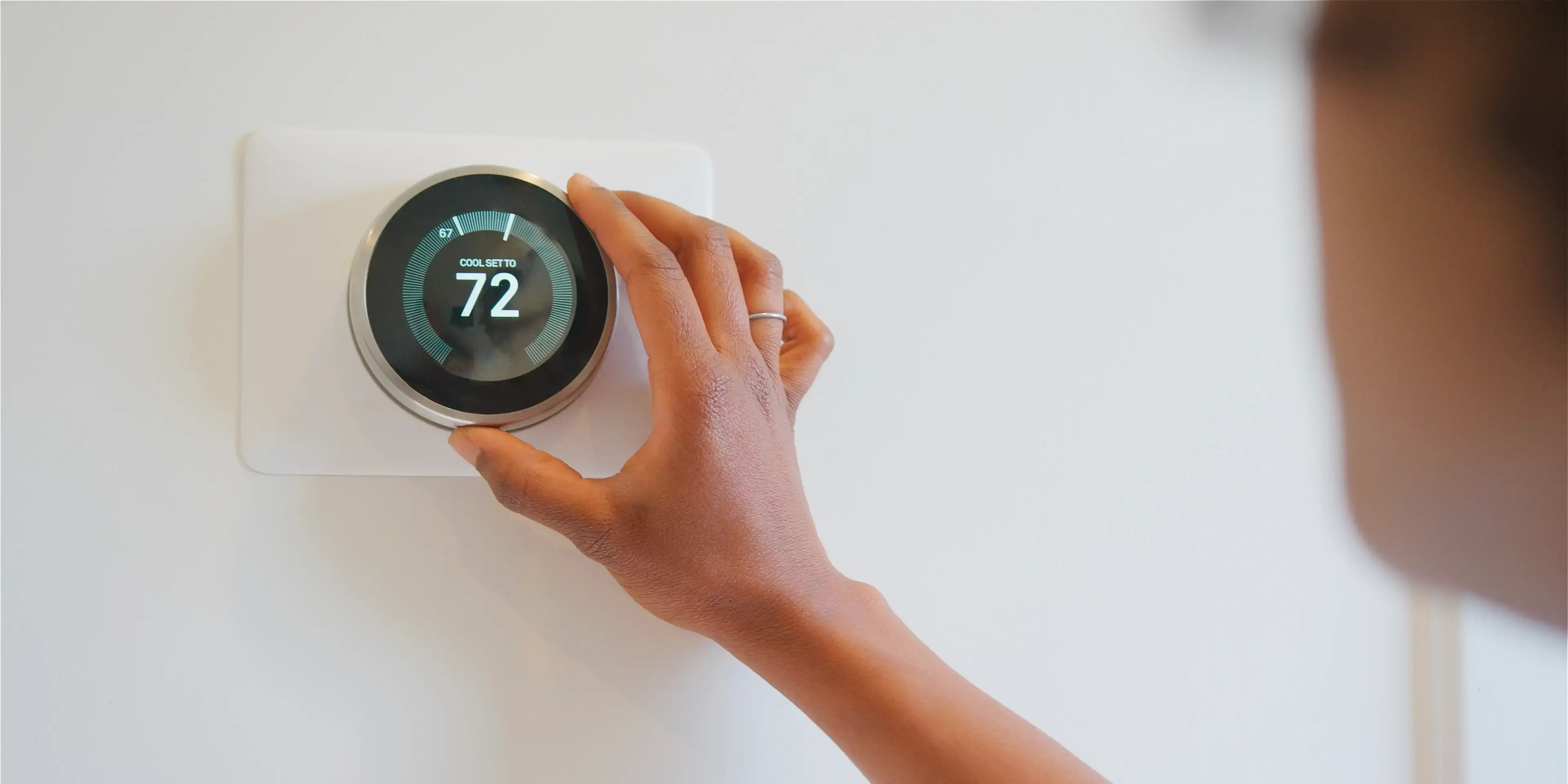 Mujer ajustando el termostato inteligente que está en la pared, como idea de domótica en el hogar