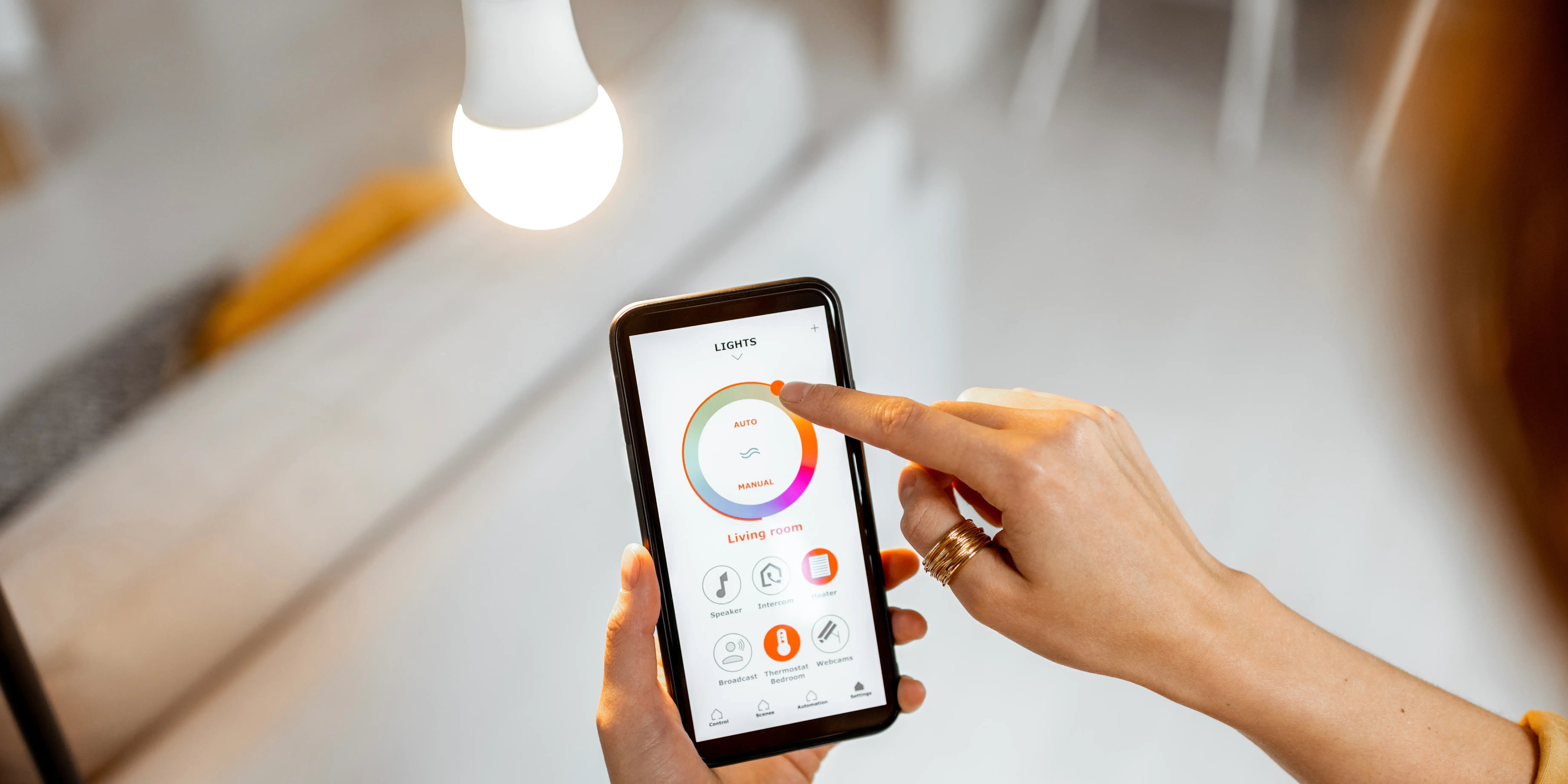 Mujer controlando la intensidad de la bombilla inteligente con una aplicación para smartphones como idea de domótica en el hogar