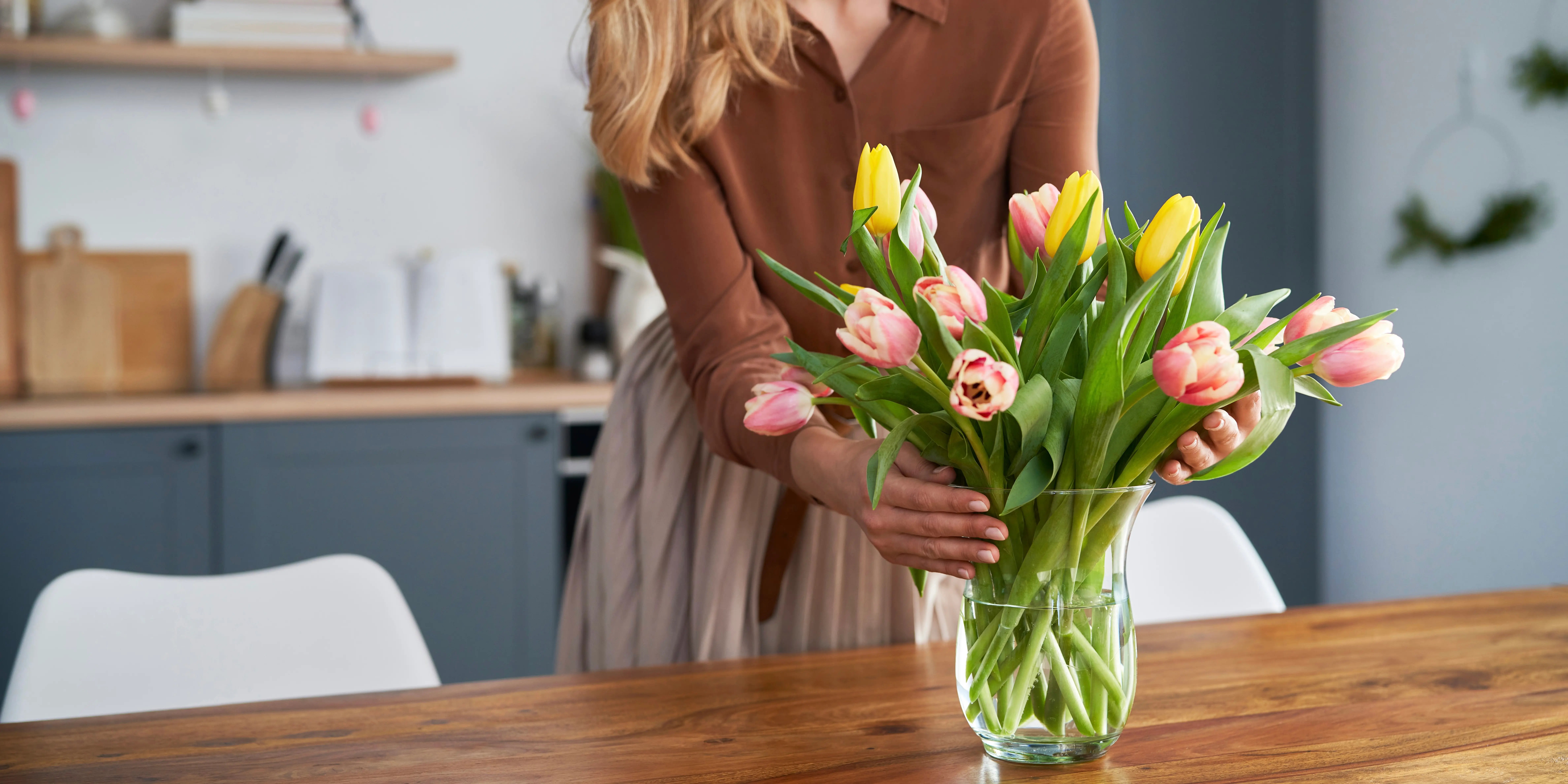 Mujer metiendo tulipanes frescos en el jarrón para incorporar plantas y crear un entorno favorable a la salud