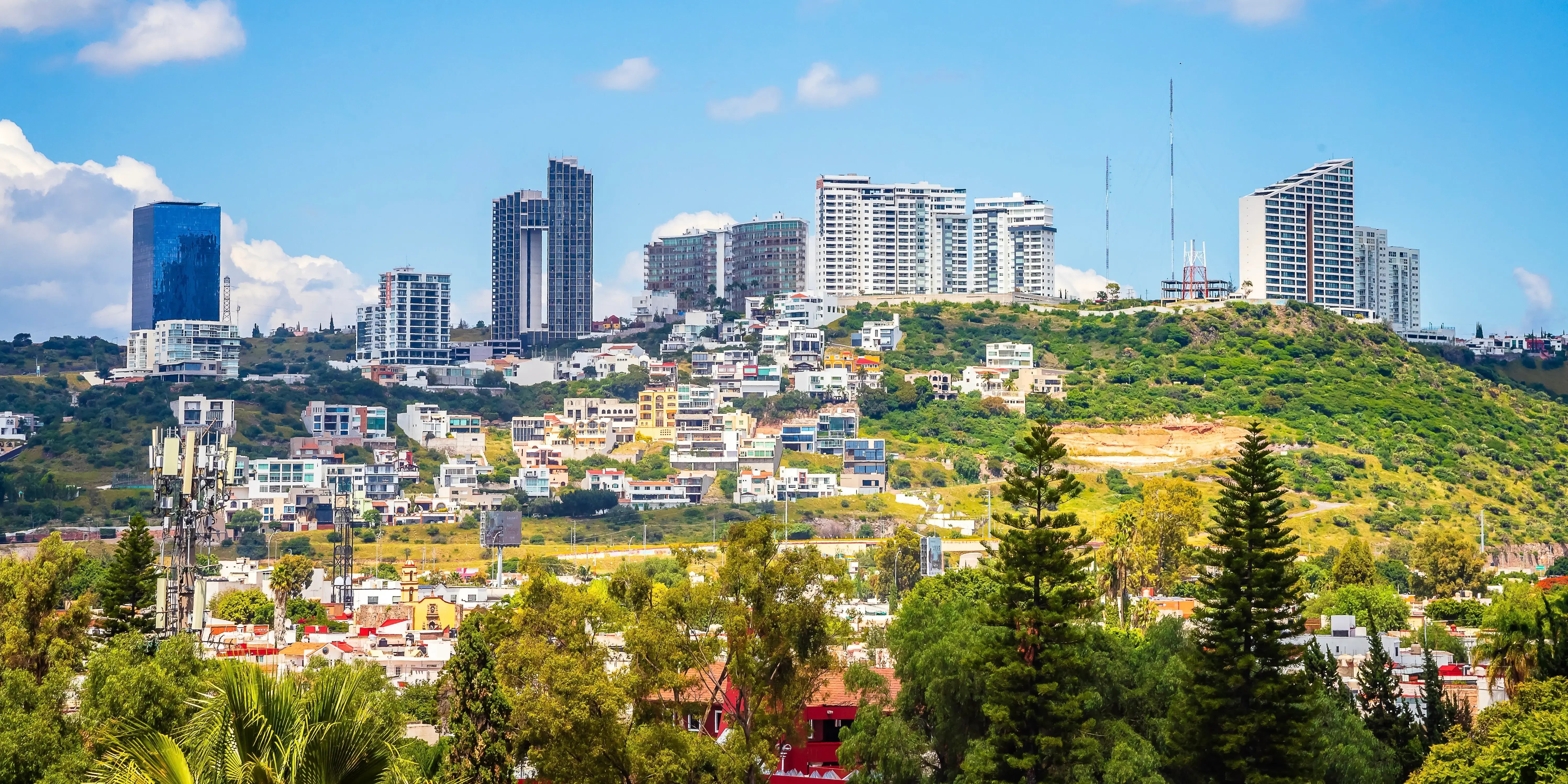Paisaje Urbana visto desde el mirador de los arcos, con edificios al fondo y un cielo azul con nubes blancas, en Querétaro