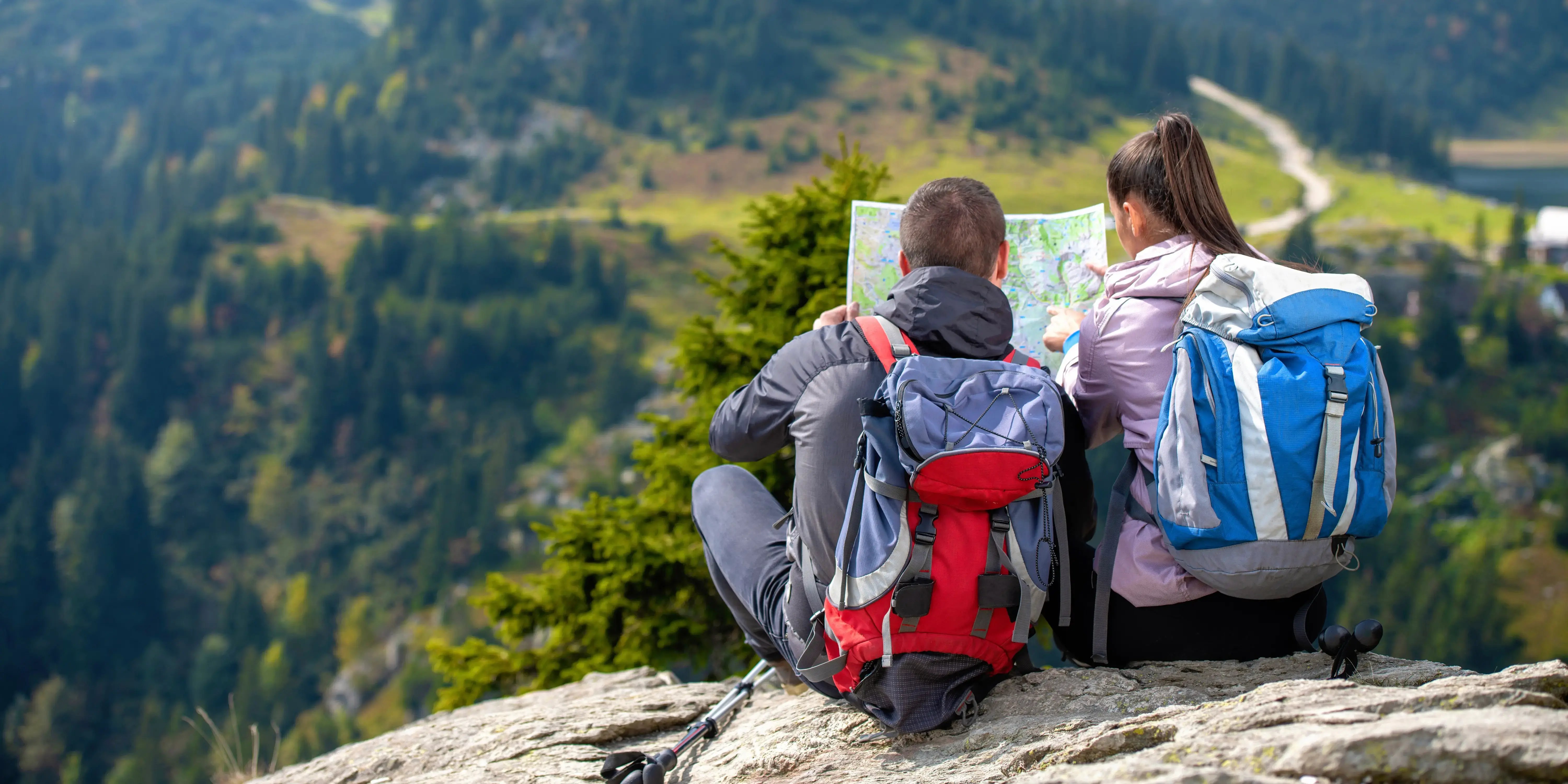 Pareja de estilo de vida aventurero sentados sobre una roca viendo un mapa