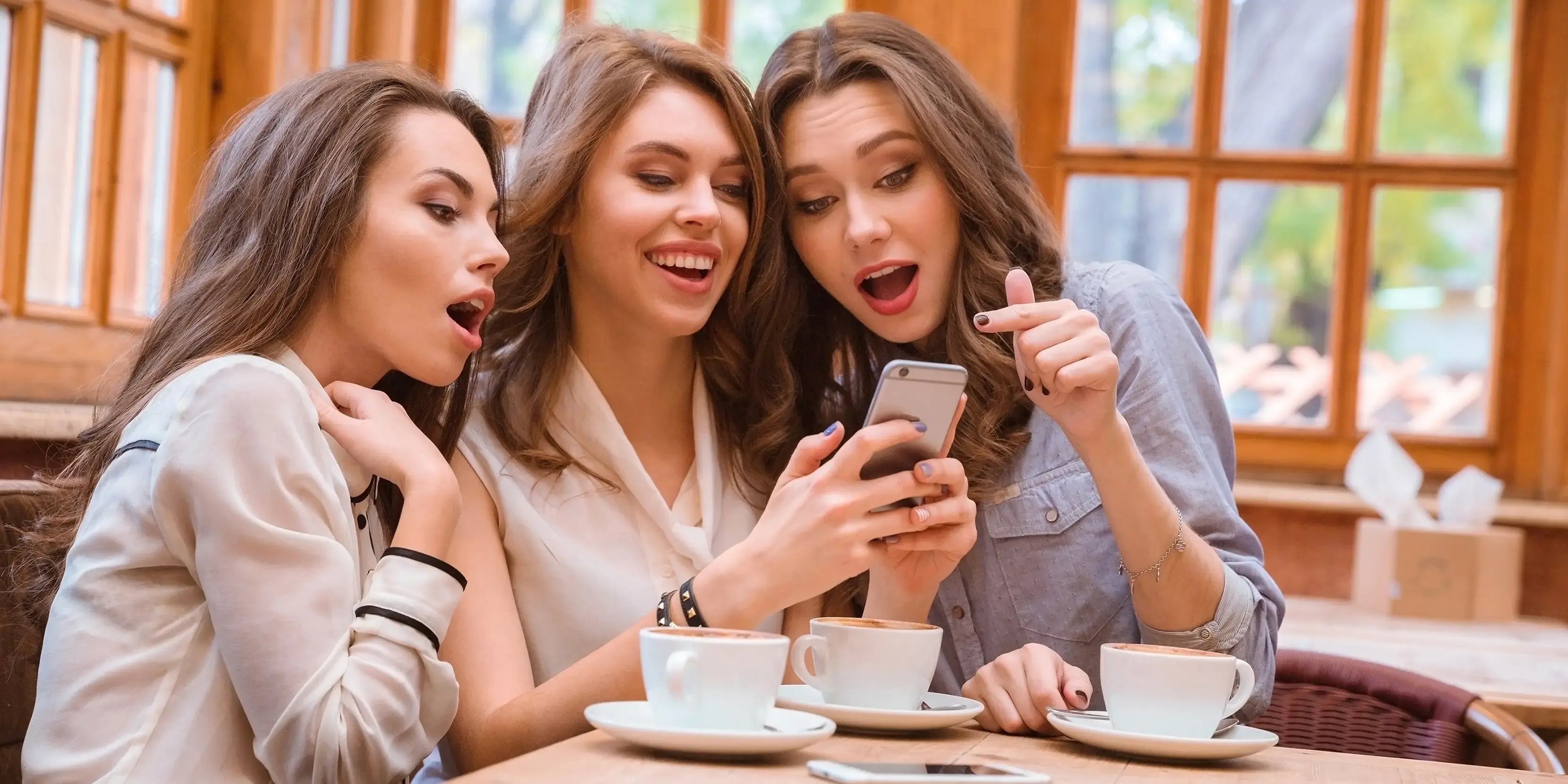 Retrato de tres mujeres alegres que usan smartphone en una cafetería en Bosque Real
