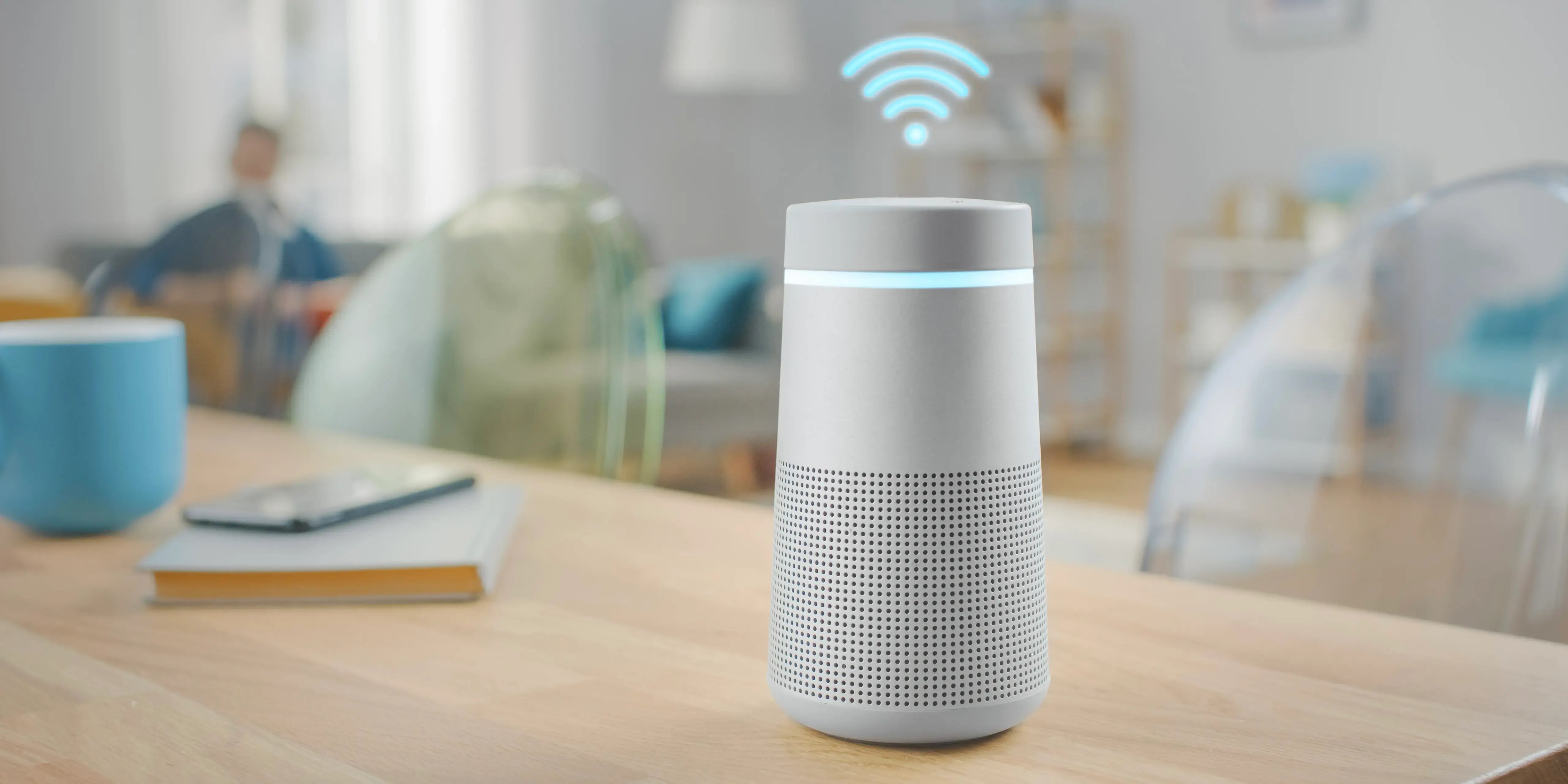 Sobre una mesa de una casa inteligente se encuentra un asistente de voz con símbolo de wifi en la parte superior